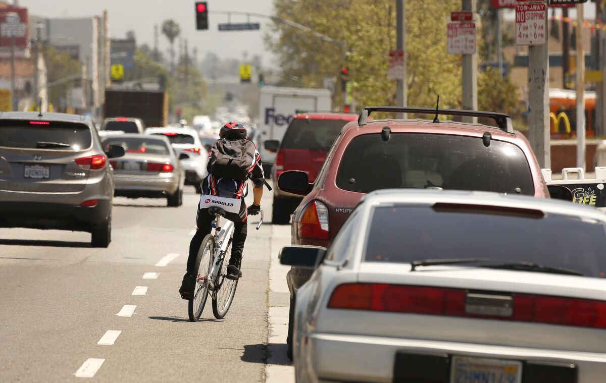 A cyclist rides next to a lane of parked cars on Manchester Avenue in South Los Angeles, one of the deadliest streets in the city for pedestrians and cyclists.