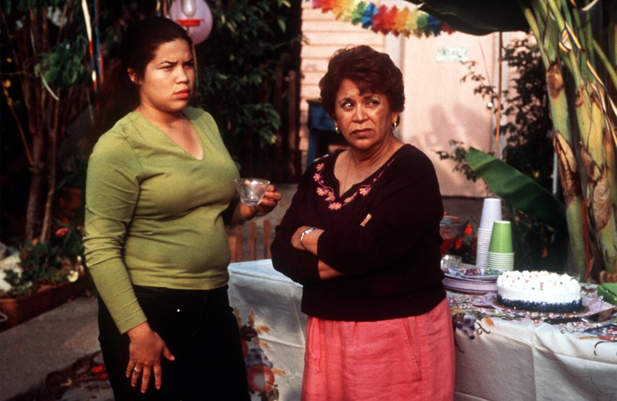 A girl and her mother stand beside a party table with a cake on it.