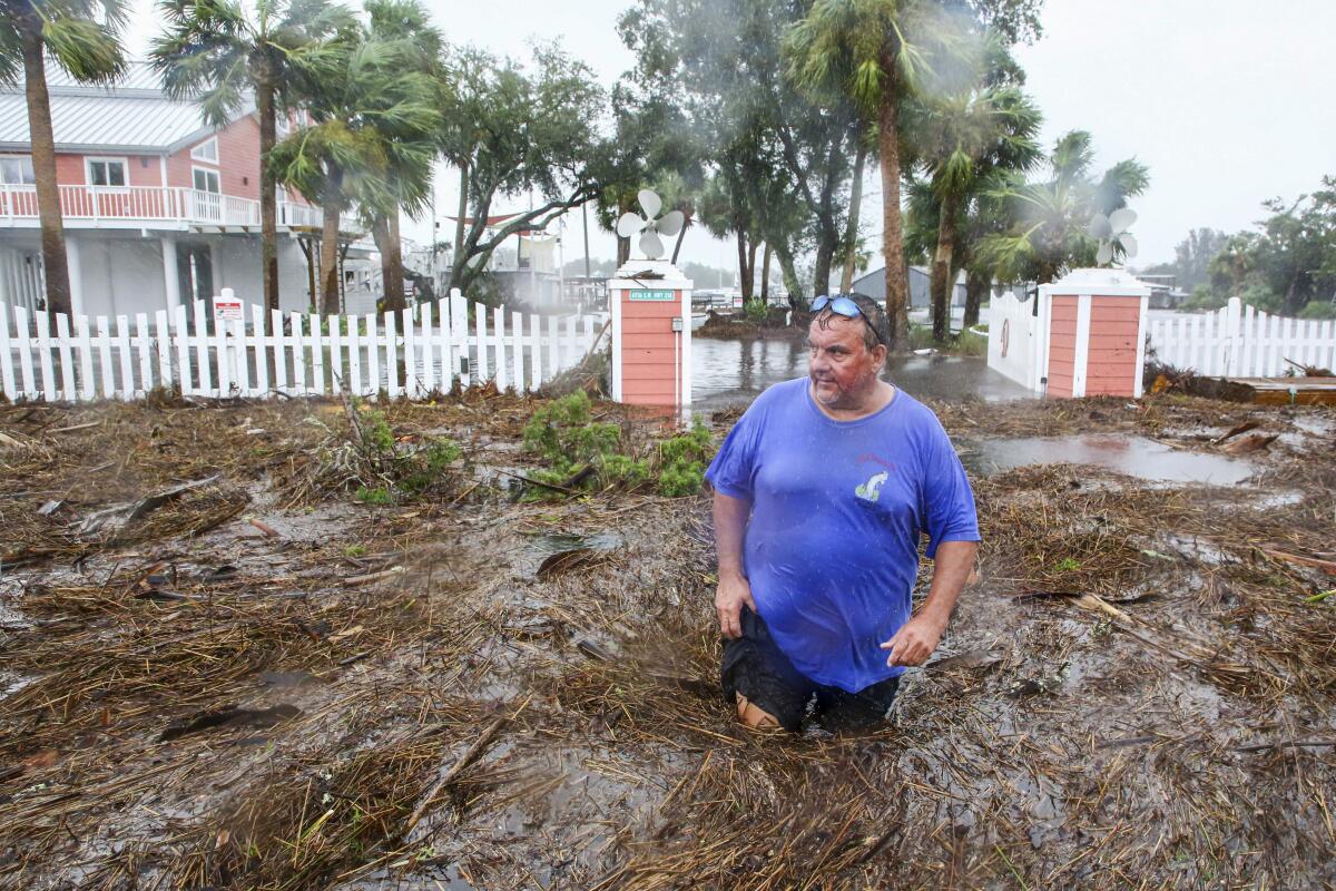 A man wades through muddy, thigh-high water in front of a home.