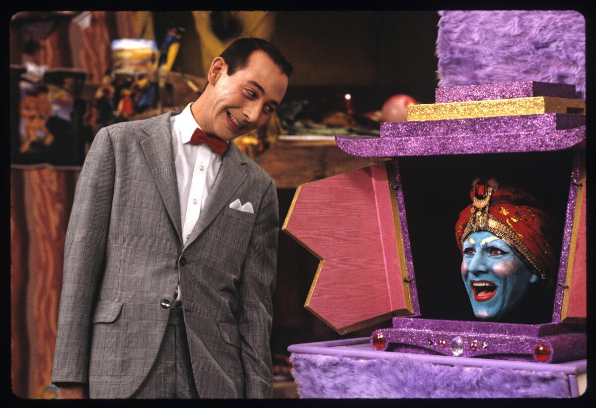 A man in a suit talks to a genie's head in a box