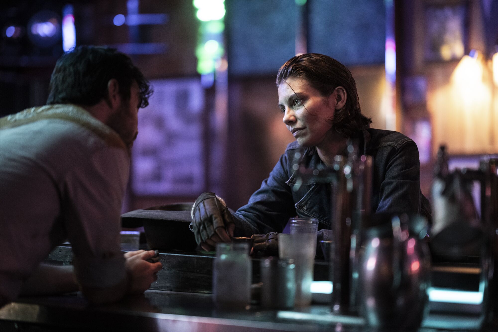 A woman sitting at a bar looks at the bartender who is leaning toward her.