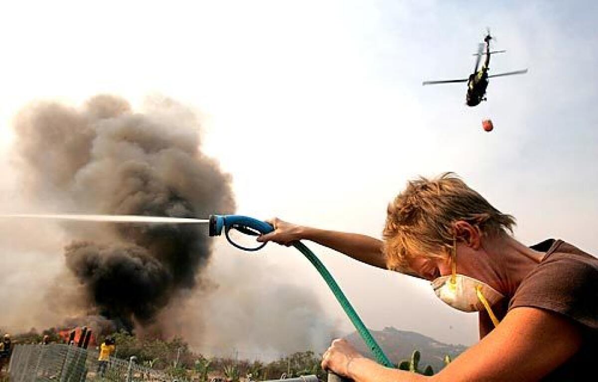 Amy Berling of Fallbrook hoses down the yard of a friend as flames approach home on Sans Souci Drive in South Escondido, Calif. on Tuesday, Oct. 23, 2007.