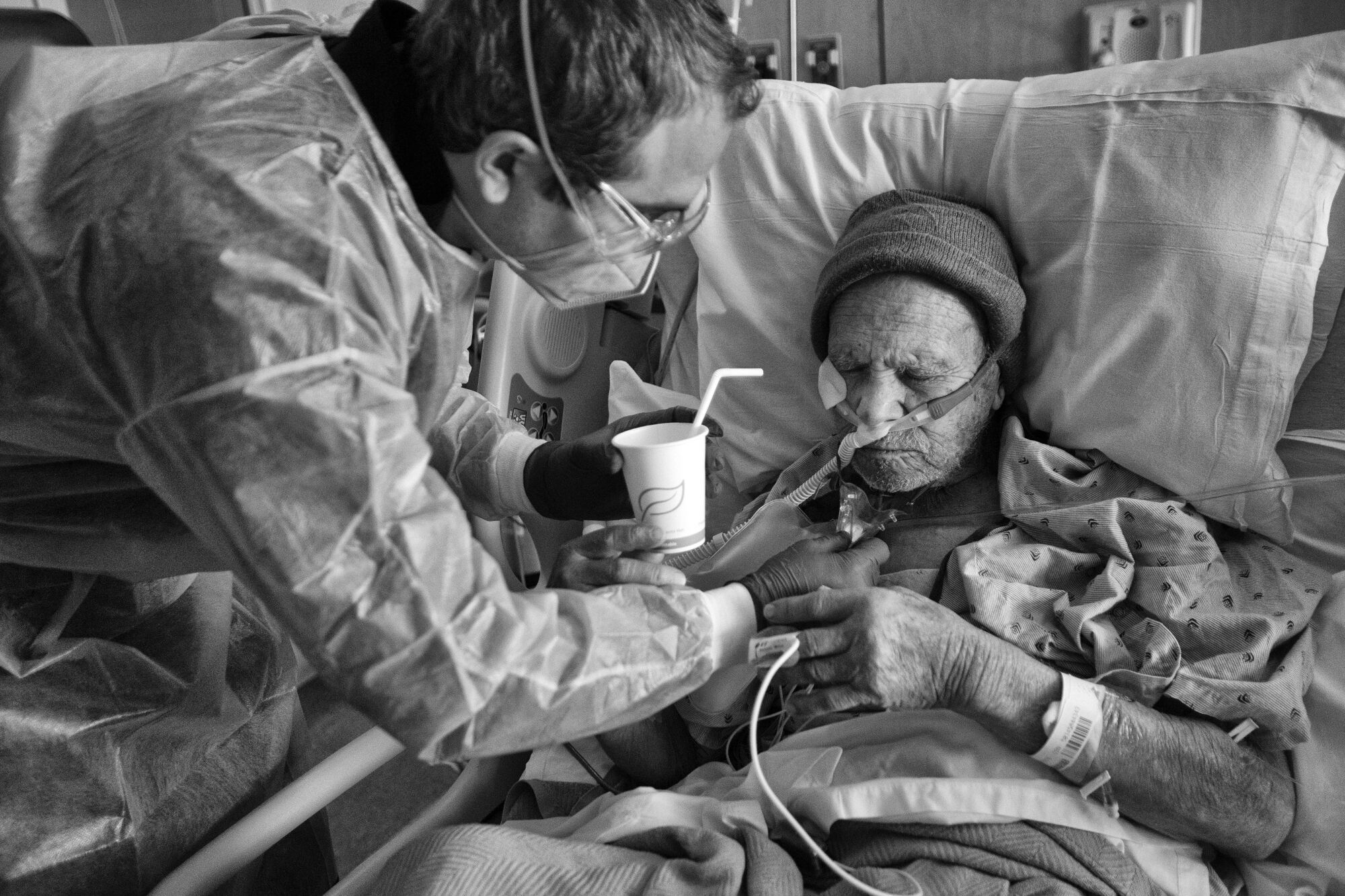 Chaplain Kevin helps a patient sip water in his hospital bed