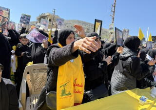A woman wearing black and a yellow banner extends a hand while standing near other people, also wearing black