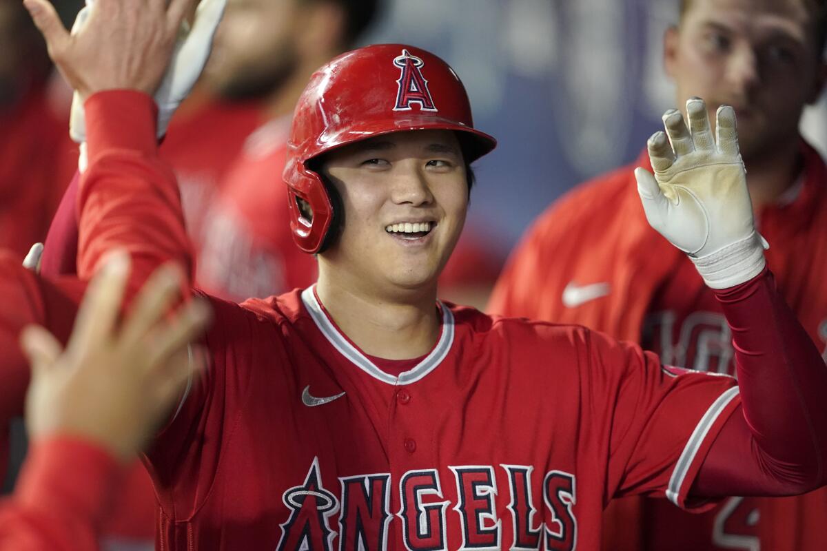 A smiling Shohei Ohtani receives high fives with both hands in the Angels' dugout after hitting a home run.