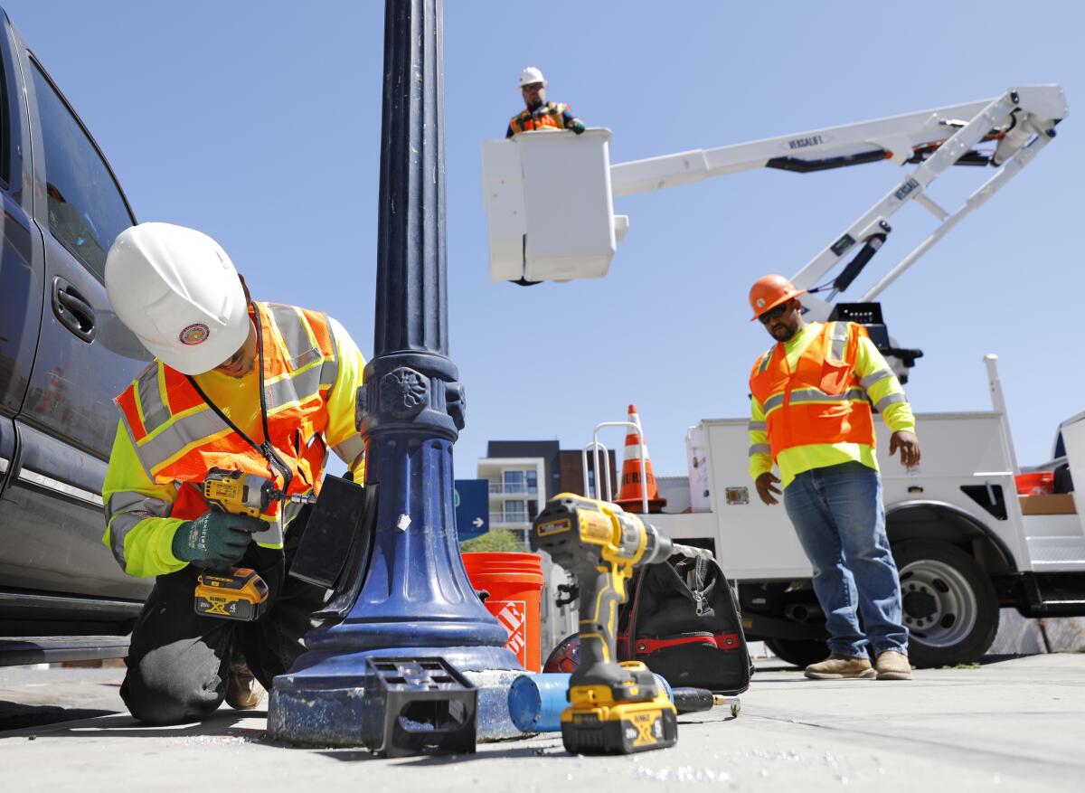 SAN DIEGO, CA - JULY 5: Contractor Israel Ruelas, left, repairs the electrical wiring on a street lamp in the East