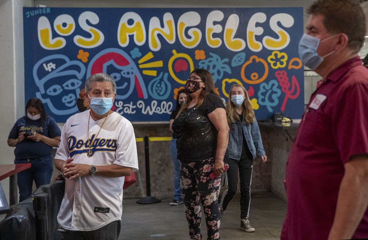 People wear masks while waiting to order food near a sign that says "Los Angeles: Eat Well."