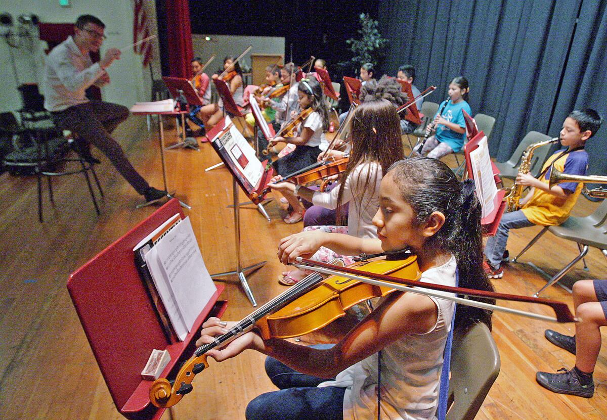In this July 2015 file photo, Alondra Cruz, 10, of Glendale, begins to play a song, following conductor Dr. Luis Zuniga's direction at the Caesura Music Camp and at Roosevelt Middle School. Caesura Youth Orchestra began in spring, and some students participated in a first summer camp that led up to a performance alongside La Sierra University music students.