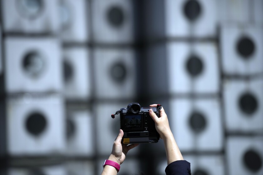 A set of hands are shown taking a photograph of the Nakagin Capsule Tower as crews begin demolition.