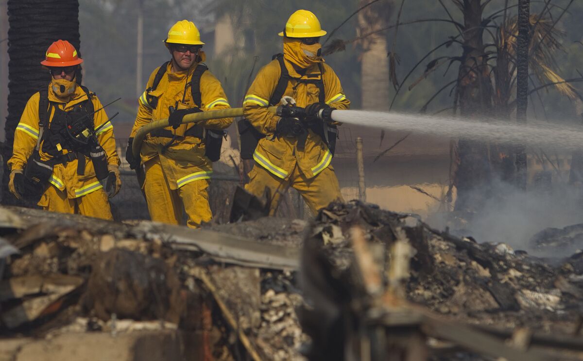 Firefighters pour water on a burning home off Country Club Drive on Thursday in the Escondido area.