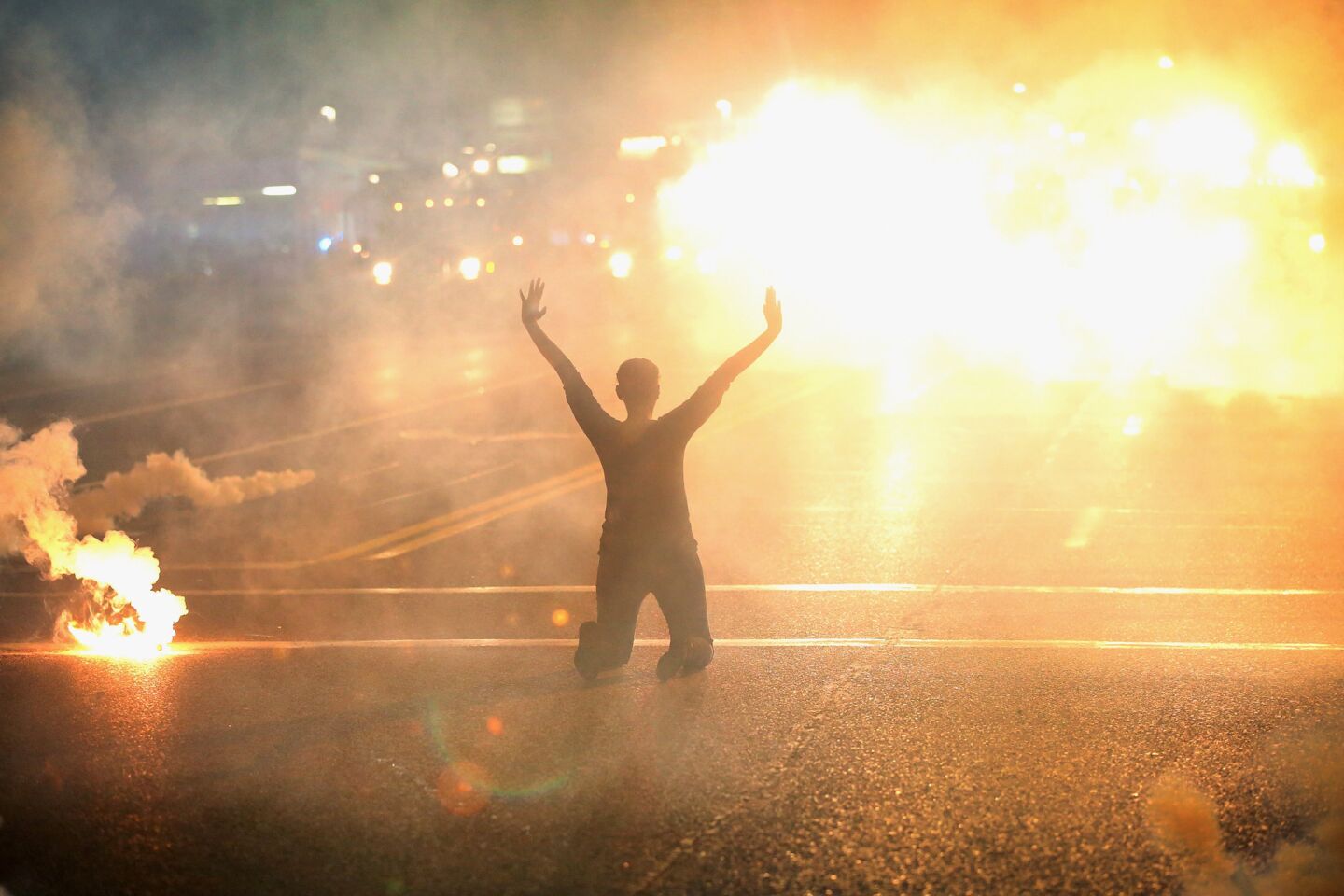 Tear gas reigns down on a woman kneeling in the street with her hands in the air in Ferguson.