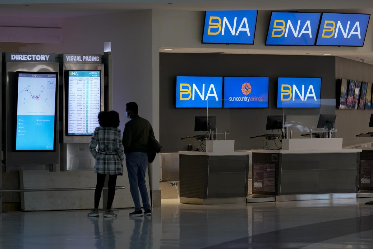 A man and woman face an electronic board inside Nashville International Airport.