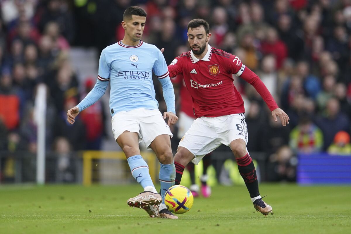Manchester City's Joao Cancelo, left, passes the ball next to Manchester United's Bruno Fernandes during the English Premier League soccer match between Manchester United and Manchester City at Old Trafford in Manchester, England, Saturday, Jan. 14, 2023. (AP Photo/Dave Thompson)