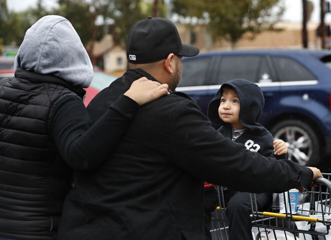 From left, Abby Neri, her husband, Juan, and her son, Damian, cover up from the rain while heading to their car after shopping at a Food4Less store in Panorama City.