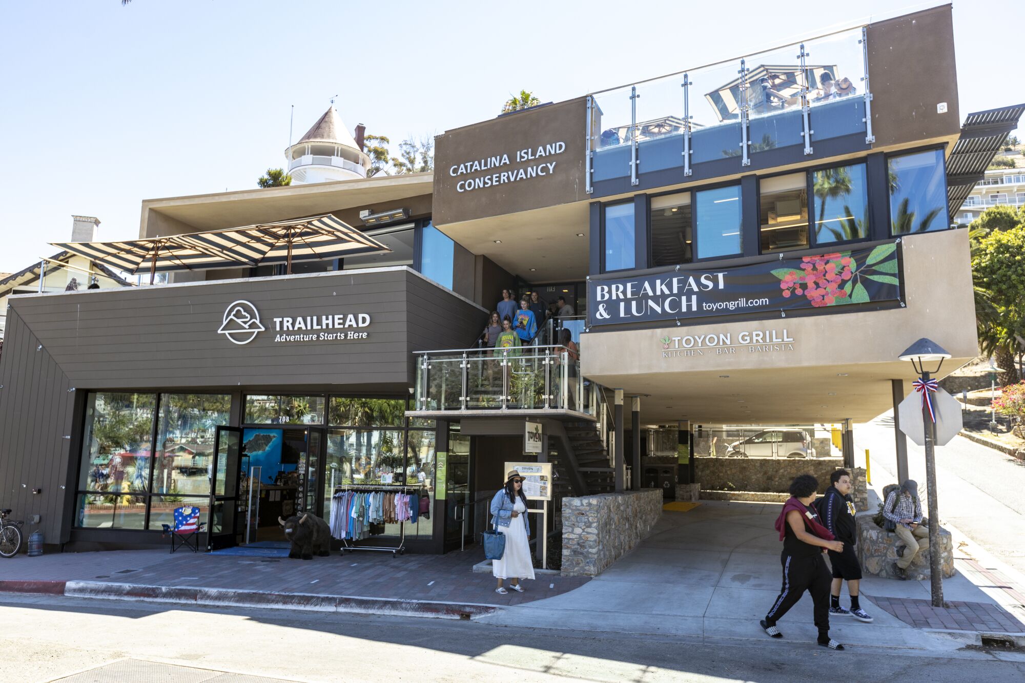 People walk past a two-story building with signs for Toyon Grill and Catalina Island Conservancy