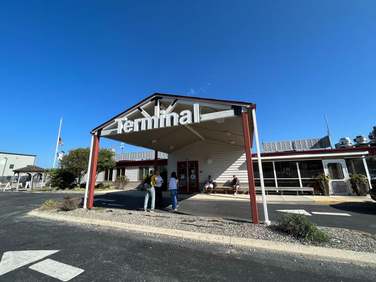 An outdoor covered entryway with the word "Terminal" overhead and people waiting underneath 