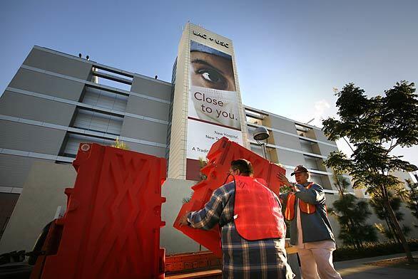 Facilities workers John Rader, right, and Carlos Herrera, left, move barriers to allow ambulances into L.A. County-USC to begin moving patients from the old facility into the new buildings.