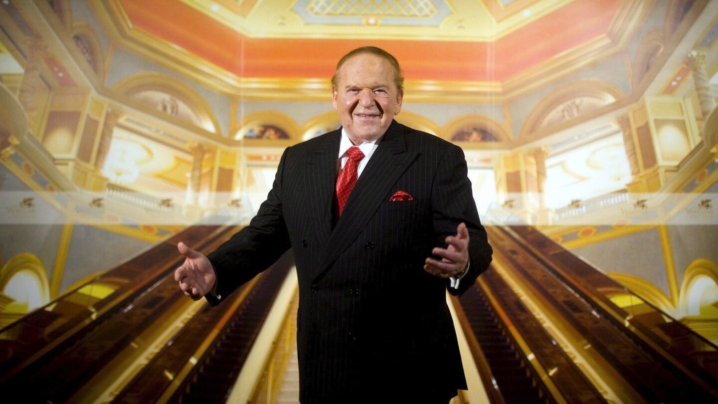 Sheldon Adelson makes a welcoming gesture with an image of a casino's escalators behind him.