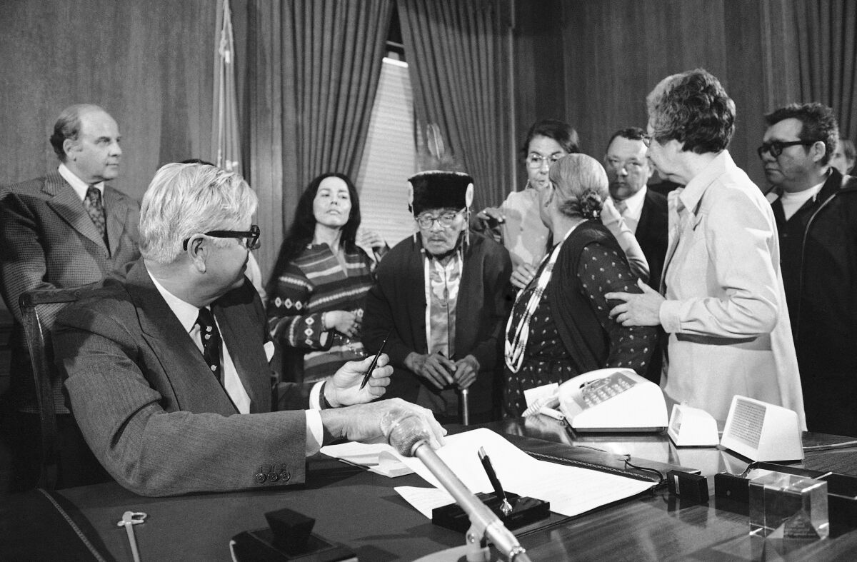 FILE - Interior Secretary Rogers Morton finishes signing a deed conveying the tribal land of the Menominee Indians of Wisconsin back to reservation status in a Washington ceremony, on April 22, 1975. The reservation status had been terminated in the early 1960s and the land converted into Wisconsin's 72nd county. From left are: Sen. Gaylord Nelson, D-Wis., Morton; Ada Deer, chairperson of the Menominee Restoration Committee; Ernest Neconish, 90, a tribal elder; an unidentified man; and Neconish's wife, Jane, 73. In 2022, Native American tribes are marking 50 years since the U.S. government's termination policy, considered an economic and human rights disaster, came to an end, making way for self-determination. More than 100 tribes were terminated under the policy, resulting in the loss of more than 1.3 million acres. (AP Photo/File)