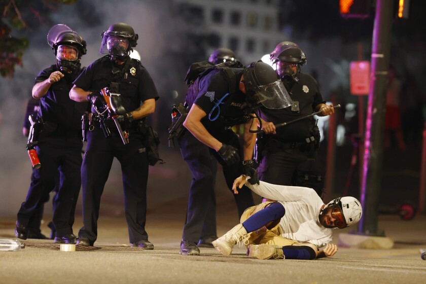 File — Denver Police Department officers clear a man who fell to the street after they used tear gas and rubber bullets to disperse a protest outside the State Capitol over the death of George Floyd, a handcuffed black man who died in police custody in Minneapolis, in this file photograph taken Thursday, May 28, 2020, in Denver. A civil lawsuit accusing Denver Police of using indiscriminate force against people protesting the killing of Floyd is set to go on trial in federal court Monday, March 7, 2022. (AP Photo/David Zalubowski, File)