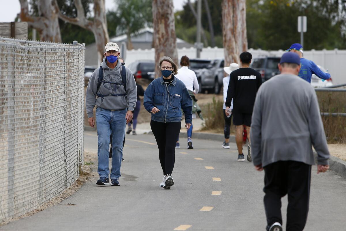 A man and women wear face masks as they walk along a path at Upper Newport Bay.