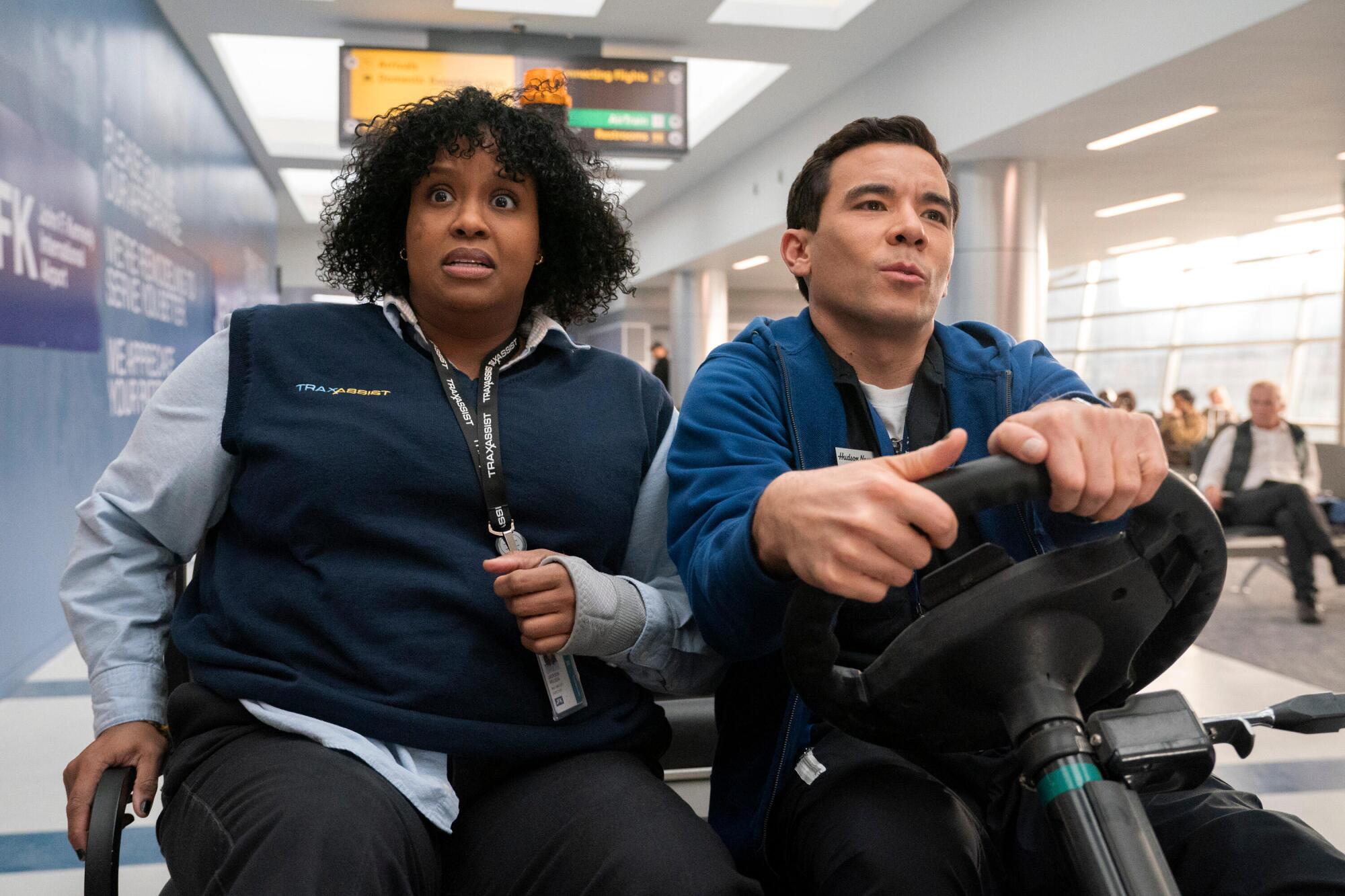 A woman and a man ride a cart through the airport.