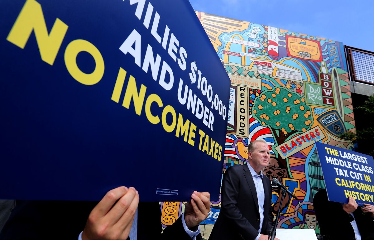 Faulconer at a news conference with a sign that reads "families $100,00 and under, no income taxes" 