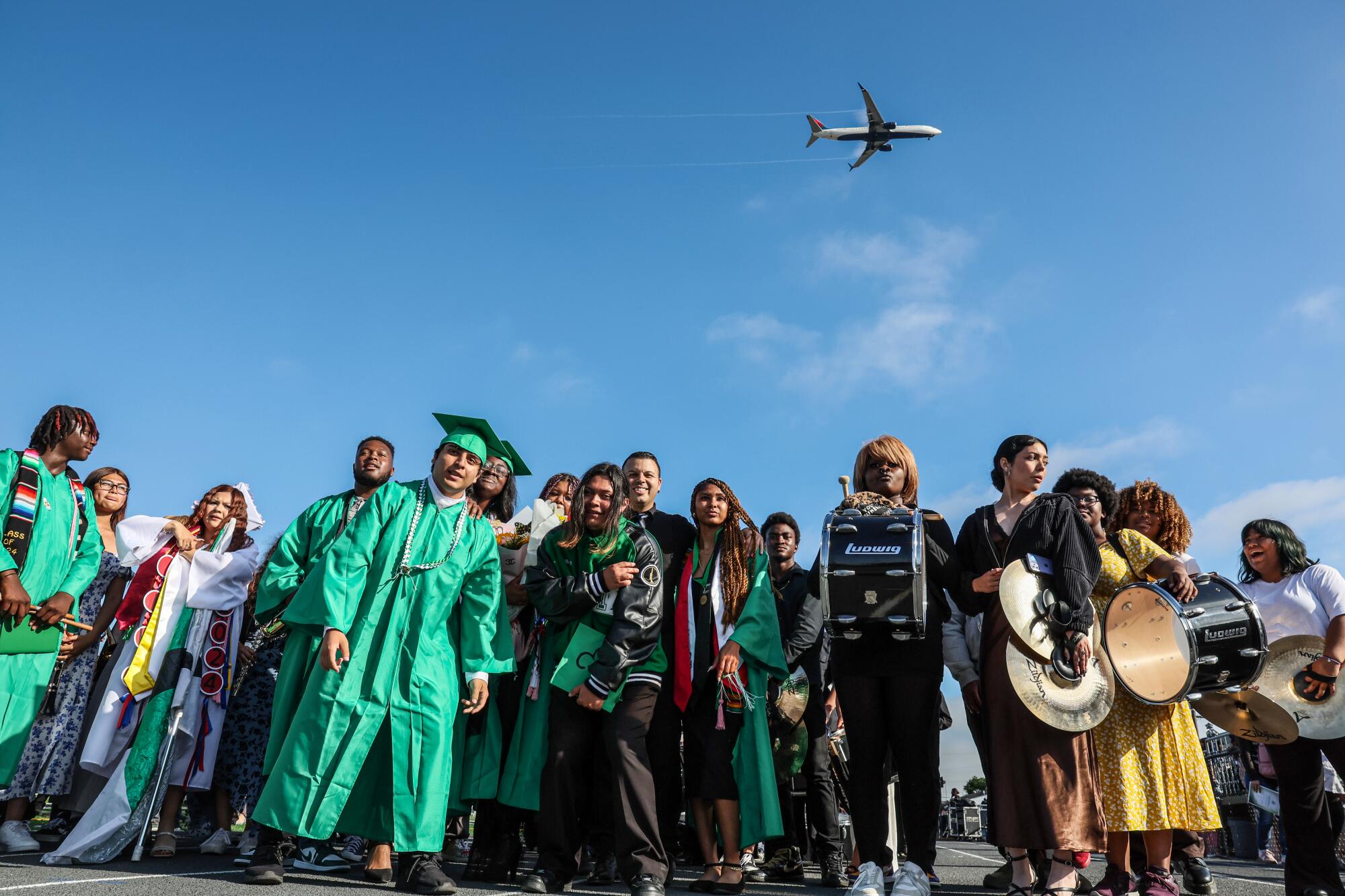 Young people, some in green robes, stand in a group outdoors.