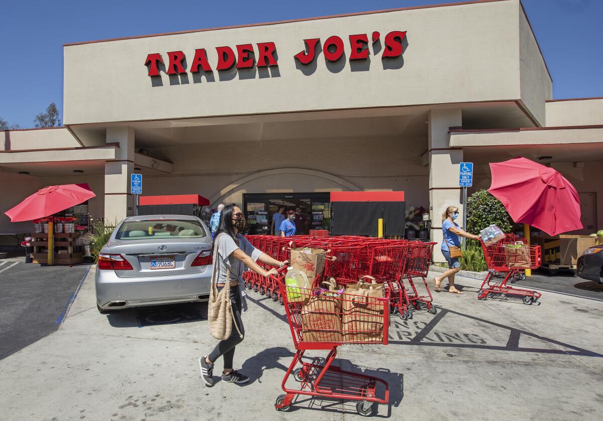 People push grocery carts in front of a building the words "Trader Joe's" on its front.