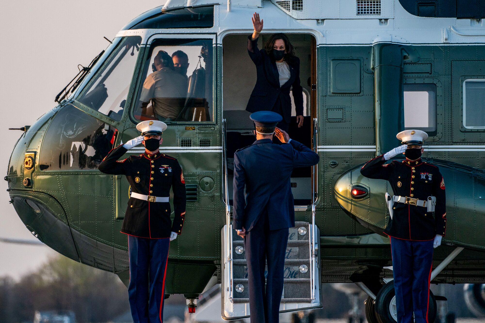 Kamala Harris waves from a helicopter as a man salutes her.