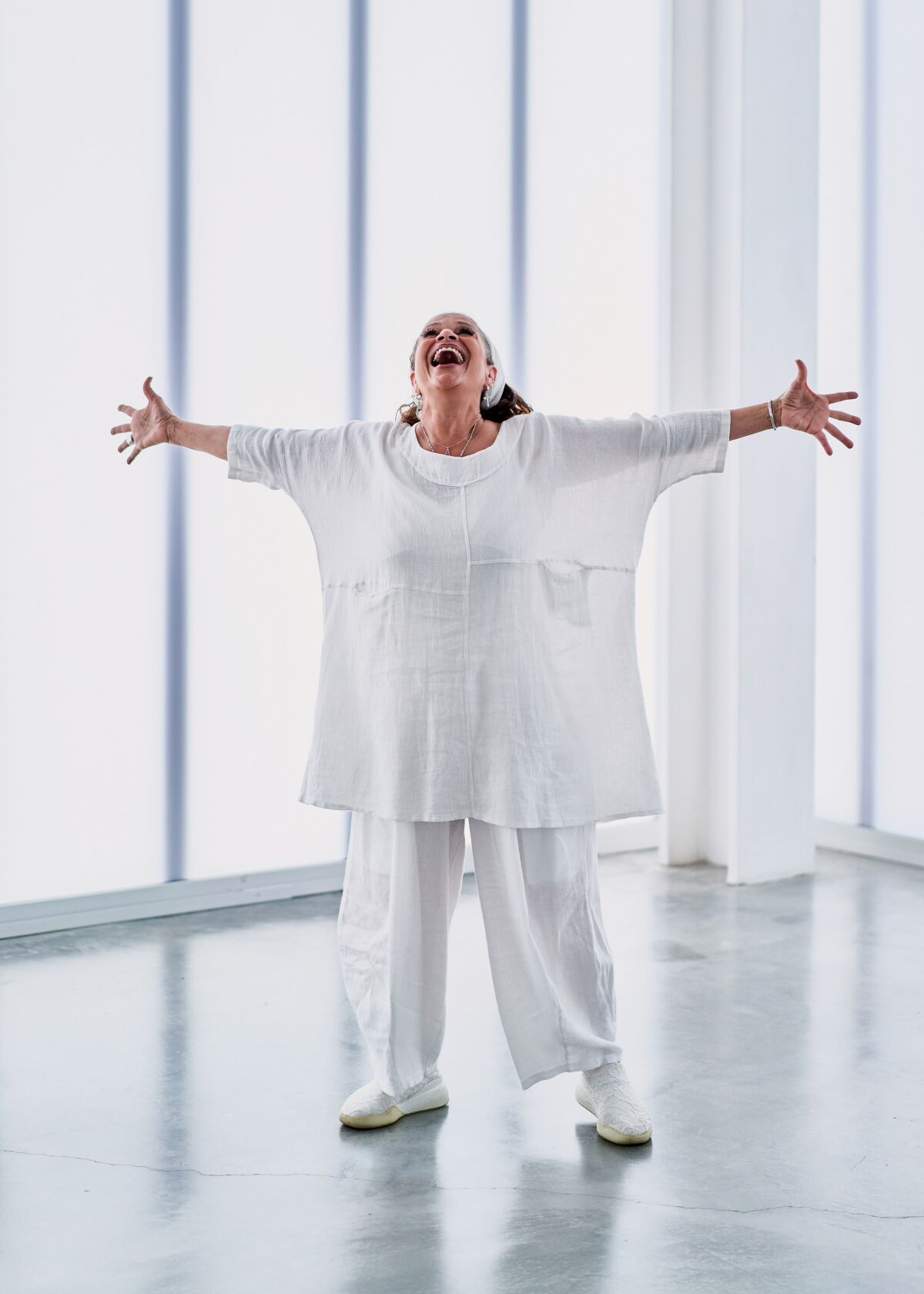 A woman wearing white reaches out her arms to her side in an expression of joy.