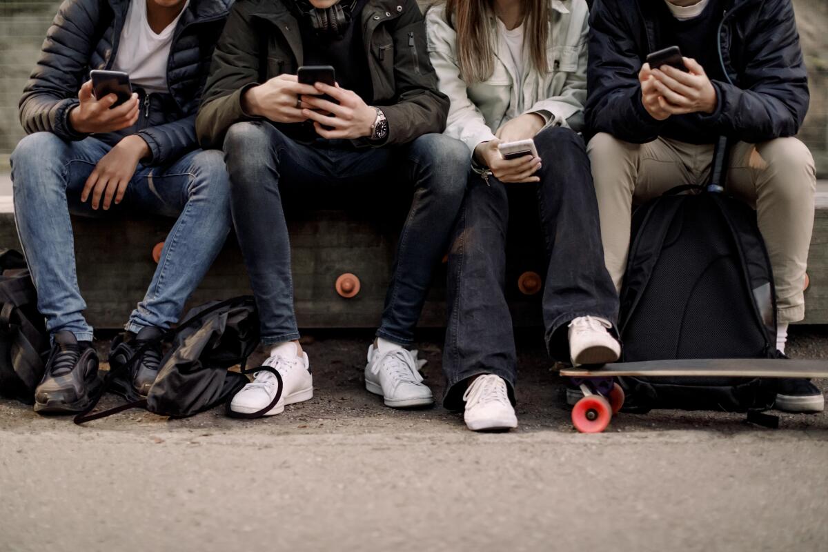 A group of teens sit next to each other, each holding a phone.