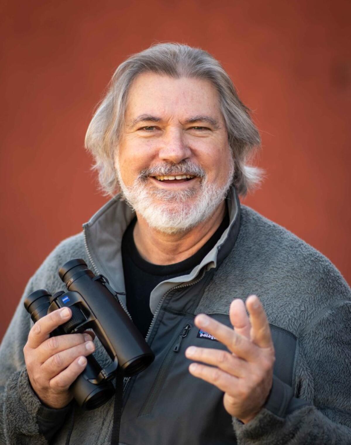 Author Charles Hood smiling and holding a pair of binoculars.