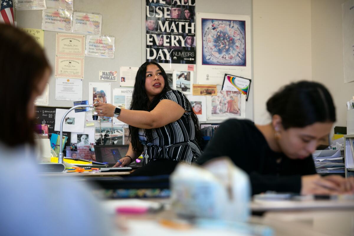 A teacher in a classroom with a poster behind her that says "We all use math every day"