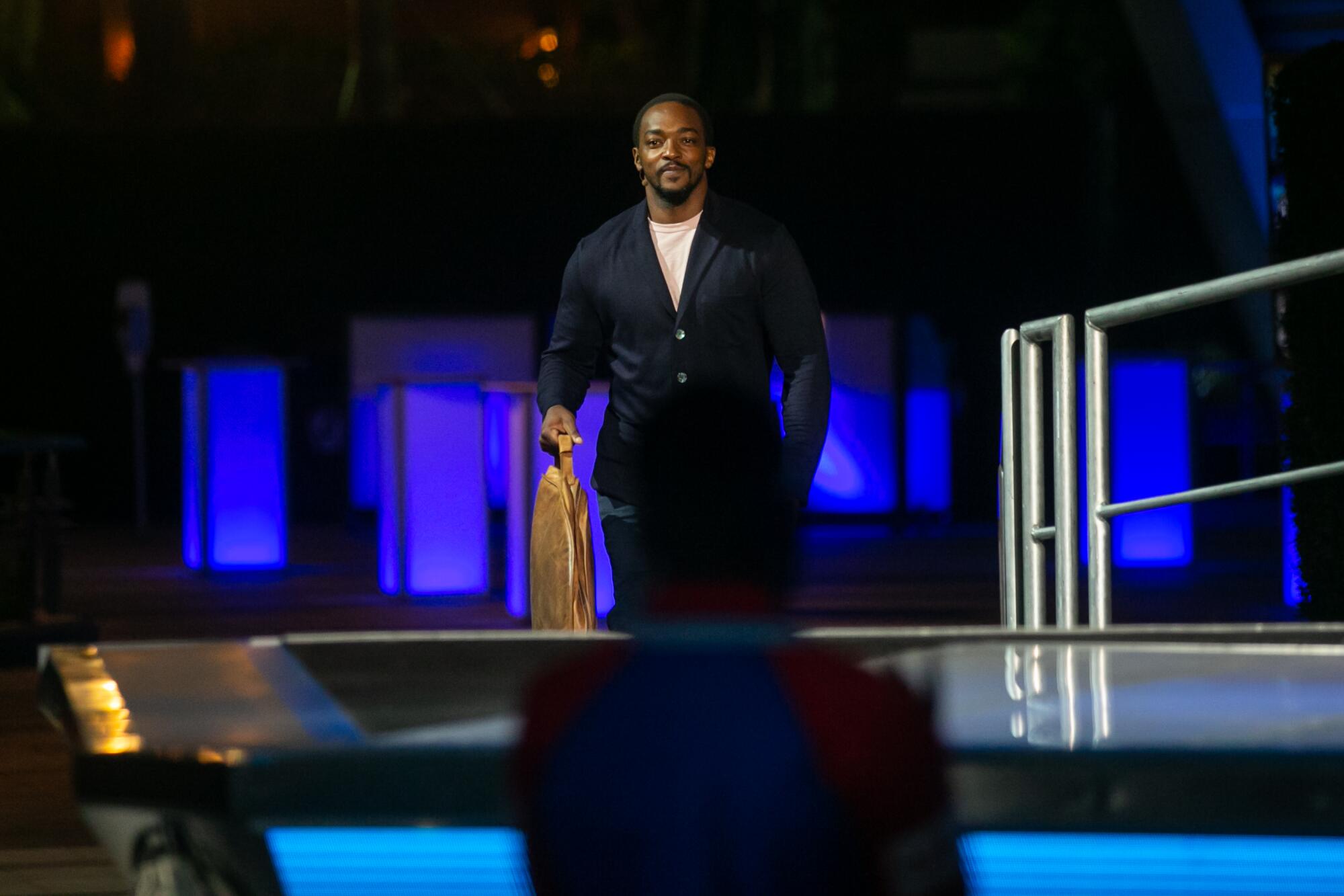 Anthony Mackie walks on stage in a dark jacket.