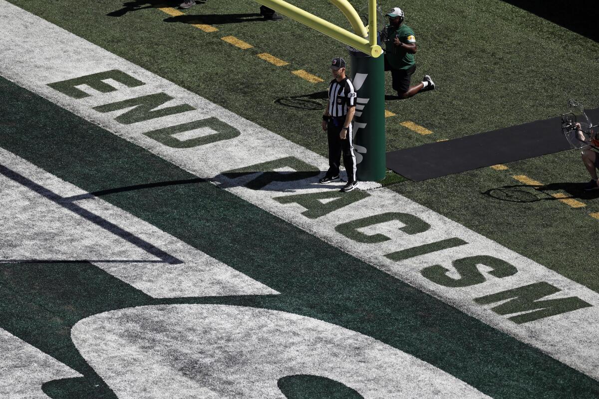 FILE - Back judge Rich Martinez stands in the end zone next to the social justice message "End Racism" as the New England Patriots take on the New York Jets during an NFL football game Sept. 19, 2021, in East Rutherford, N.J. NFL teams will stencil “It Takes All of Us” and “End Racism” in end zones for the third straight season as part of the league’s Inspire Change social justice initiative. Players again can wear specific messages on their helmets. (AP Photo/Adam Hunger, File)