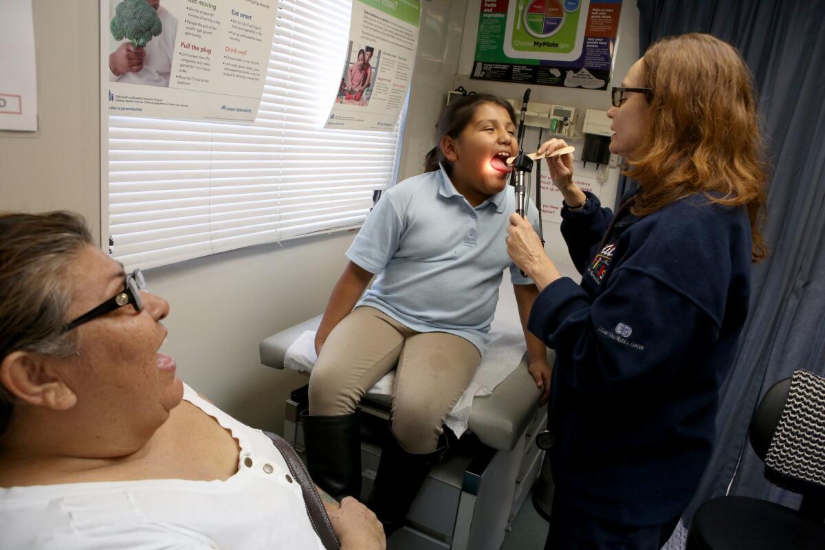 Carmen Sanchez, left, watches as her 8-year-old daughter Dafne is examined by nurse practitioner Anne Traynor in a Cedars Sinai mobile clinic visiting Jordan Down housing project in Los Angeles in January.