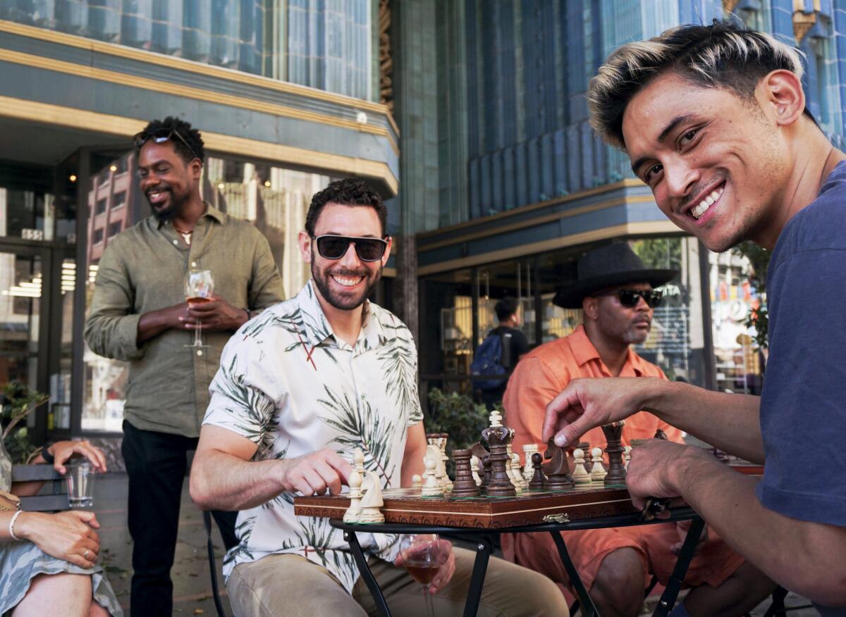 Smiling men sit at a table over a chess board.