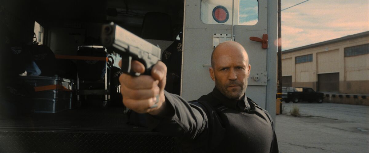 Jason Statham holds and points a gun.
