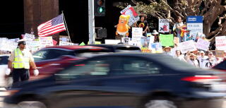 Protesters hold signs and the U.S. flag outside the Wilshire Federal Building.