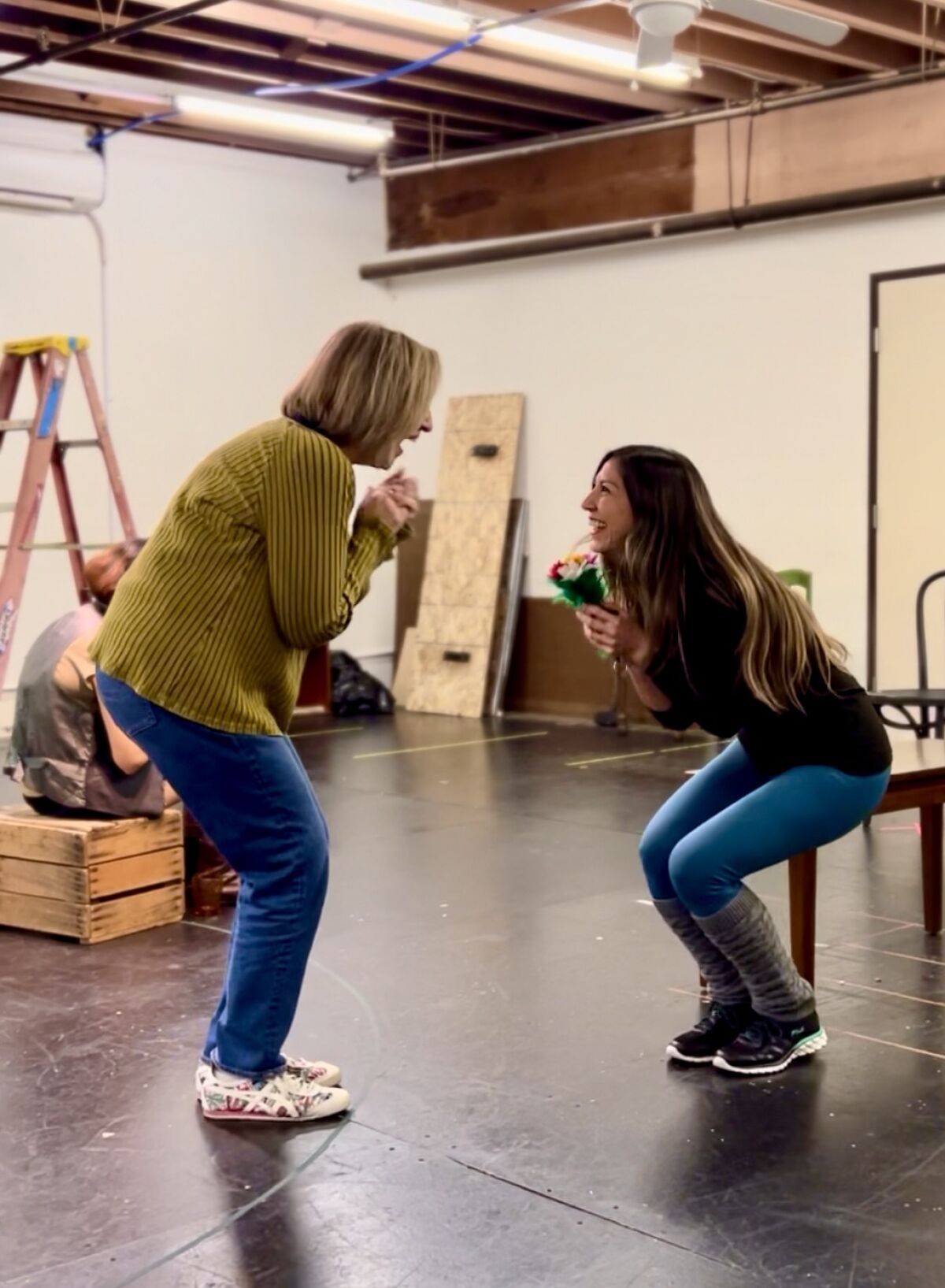 Two women in street clothes talk excitedly while rehearsing a scene