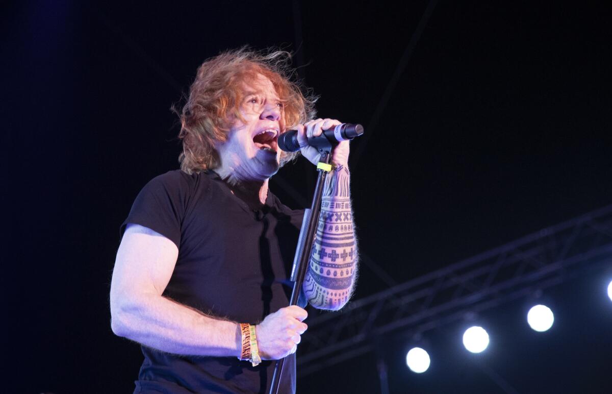 A male singer in a black t-shirt performs onstage.