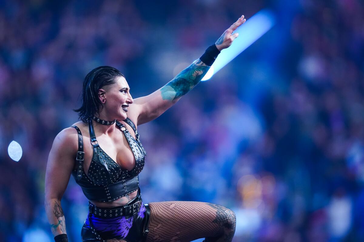 A woman in gladiator-style bikini extends her arm onstage before a crowd of fans