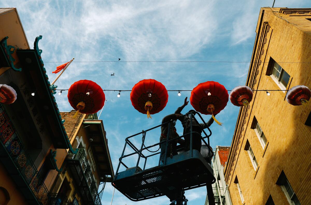 Seen from beneath, workers reach toward red lanterns suspended across a street.
