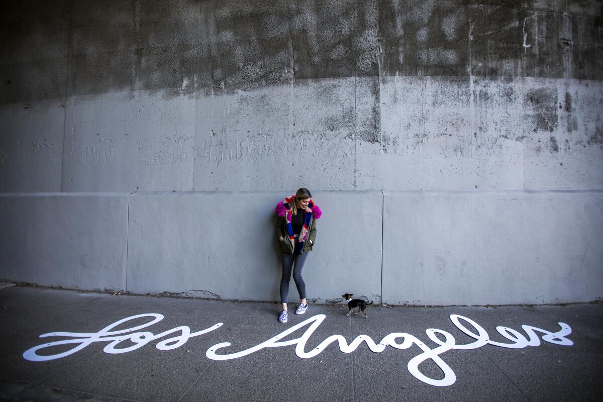 Tory DiPietro and her chihuahua stand by the words "Los Angeles" in a white script aluminum cutout.