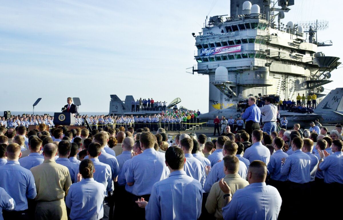 A crowd faces George W. Bush, who stands at a podium on an aircraft carrier.