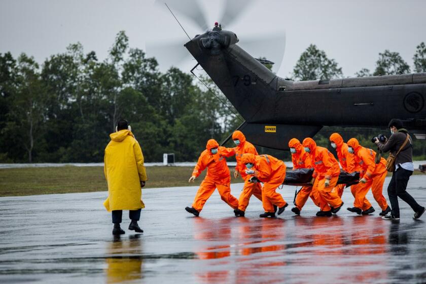 Search and rescue team members carry the body of an AirAsia Flight 8501 crash victim from a Singaporean navy helicopter in Surabaya, Indonesia, on Sunday.