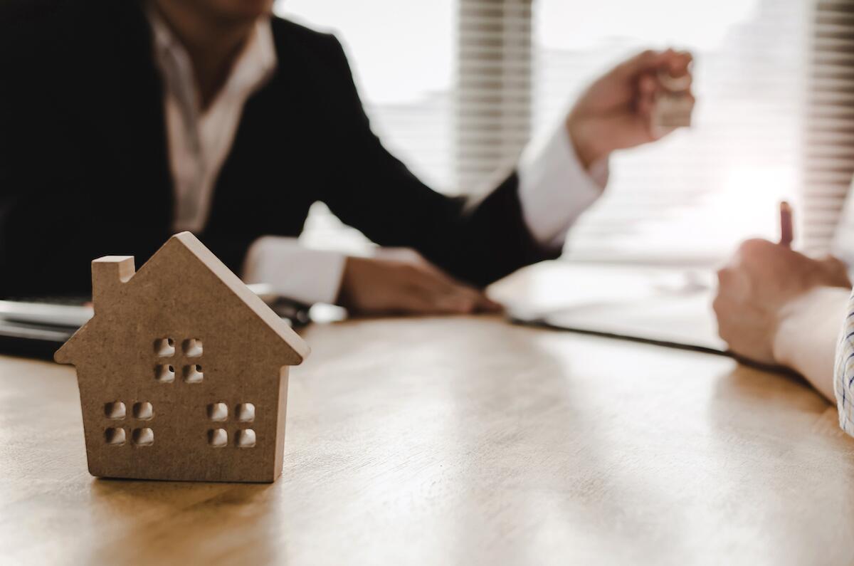 Hands exchanging keys, while on a table is a cutout depicting a home.