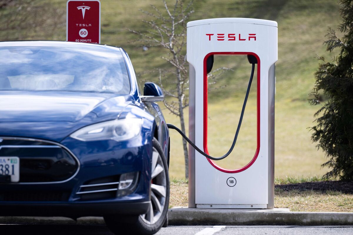 A Tesla Model S sedan is plugged into a Tesla Supercharger electrical vehicle charging station 