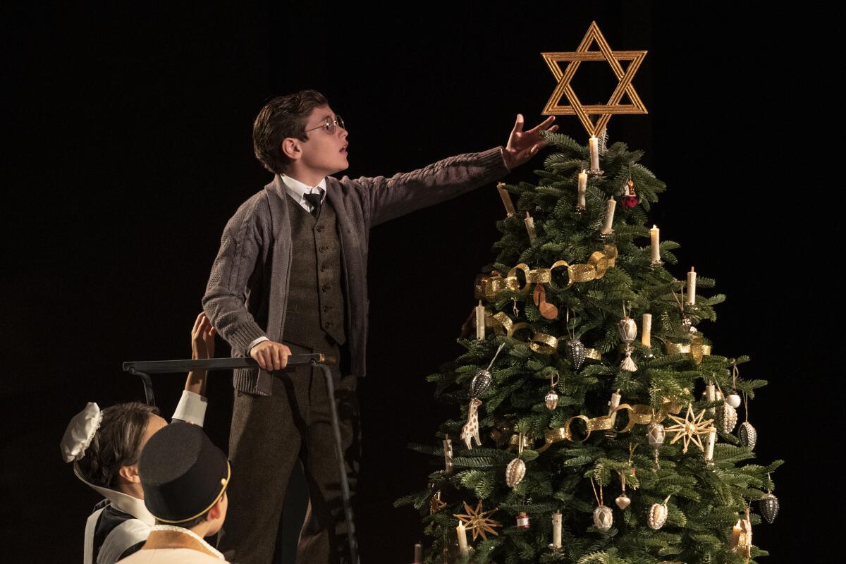 A boy places a Star of David atop a Christmas tree.